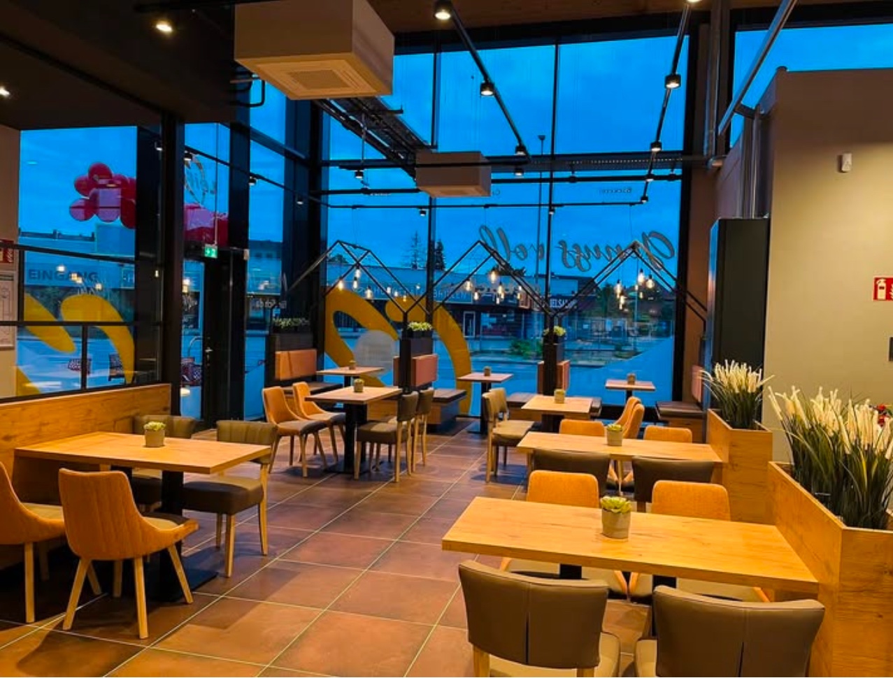 Café mit Holztischen, Sitzbänken und gepolsterten Stühlen
